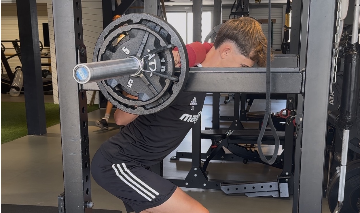 Un sportif réalise un squat avec une barre dans la salle du Zanotti Center